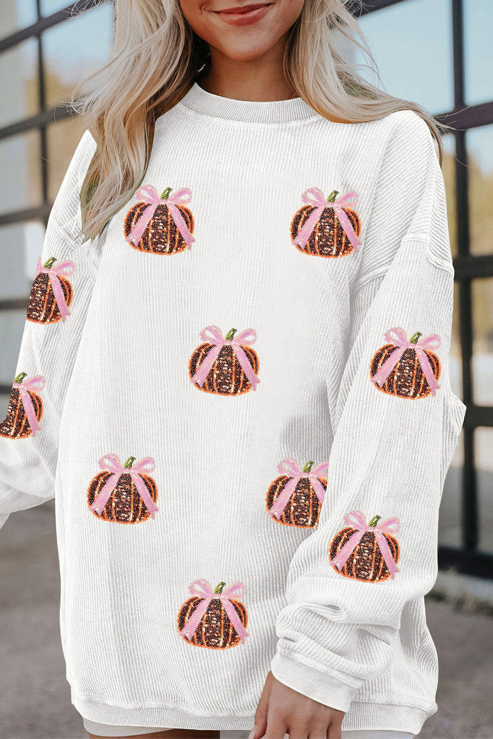 White sweatshirt with pumpkin designs and pink bows worn by a person.