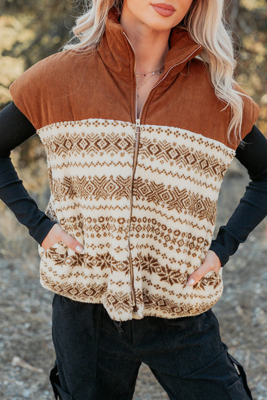 A woman wearing a brown and cream patterned fleece vest over a black long-sleeve top and black pants, photographed outdoors with a blurred natural background.