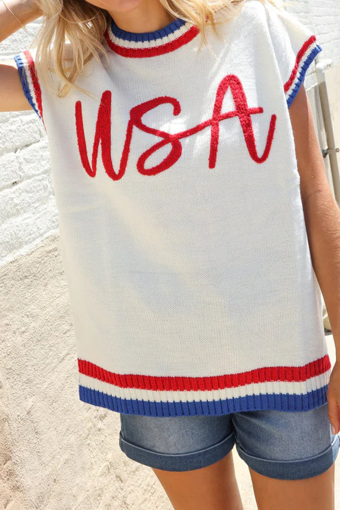 Person wearing a sleeveless sweater with 'USA' text and blue shorts on a light background