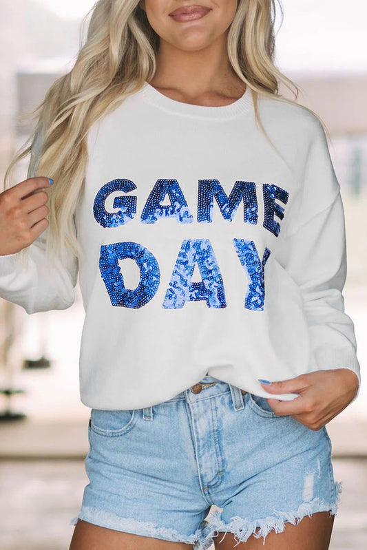 Person wearing a white sweatshirt with 'GAME DAY' in blue sequins and denim shorts.