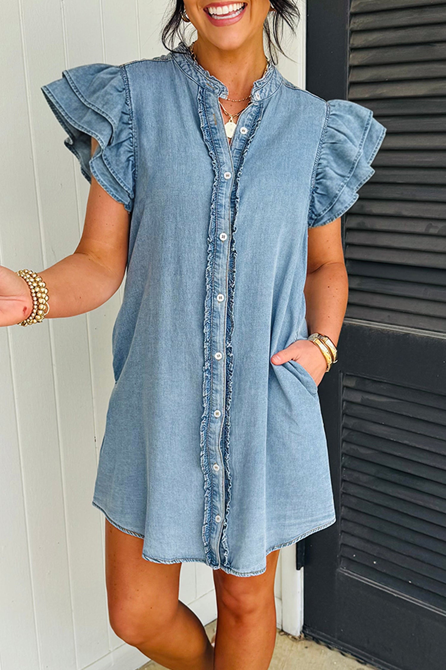 Woman wearing a denim dress with ruffled sleeves in front of a white wall.