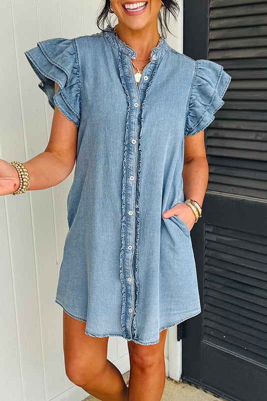 Woman wearing a denim dress with ruffled sleeves in front of a white wall.