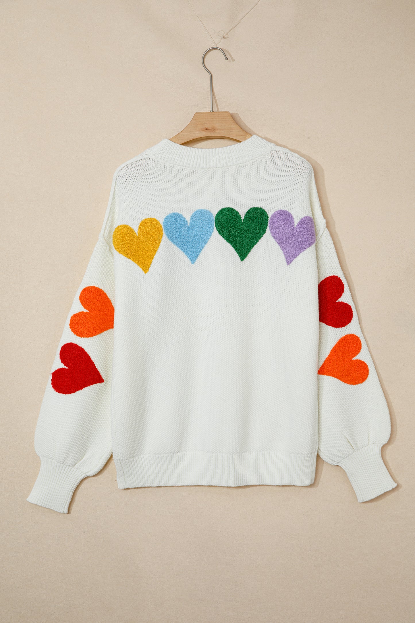 White sweater with colorful heart patterns on a beige background