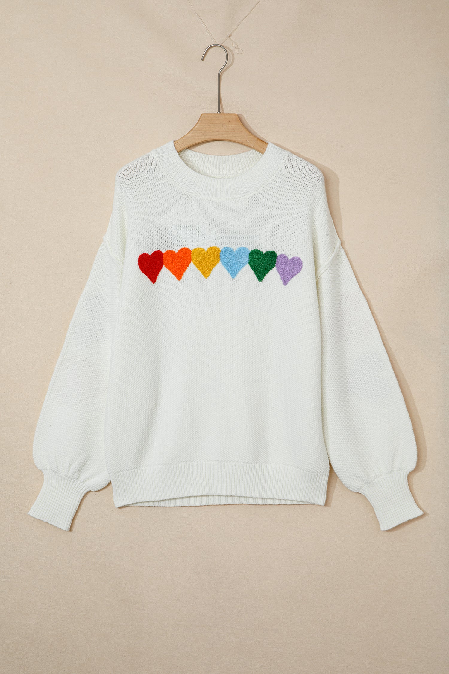 White sweater with rainbow heart design on a beige background