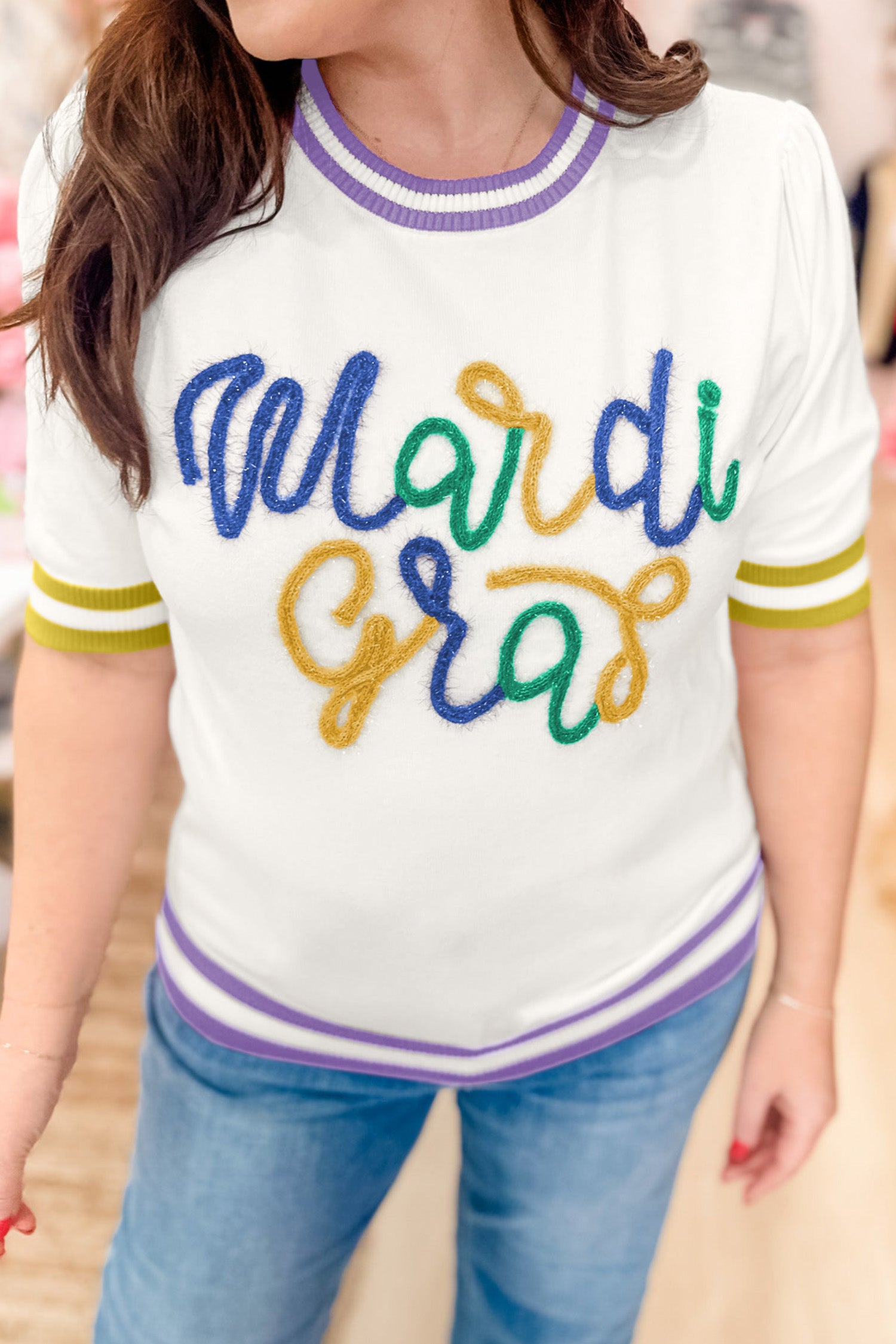 Person wearing a white t-shirt with 'Mardi Gras' in colorful letters.