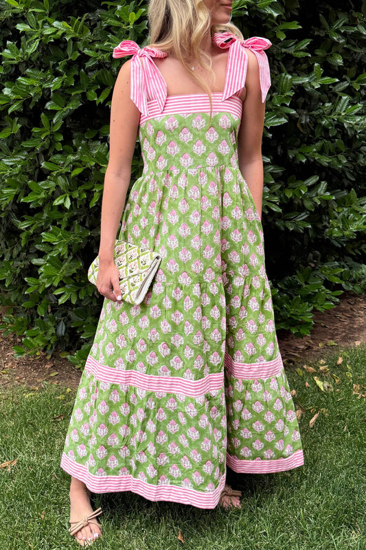 Woman wearing a green floral dress with pink accents against a green bush background